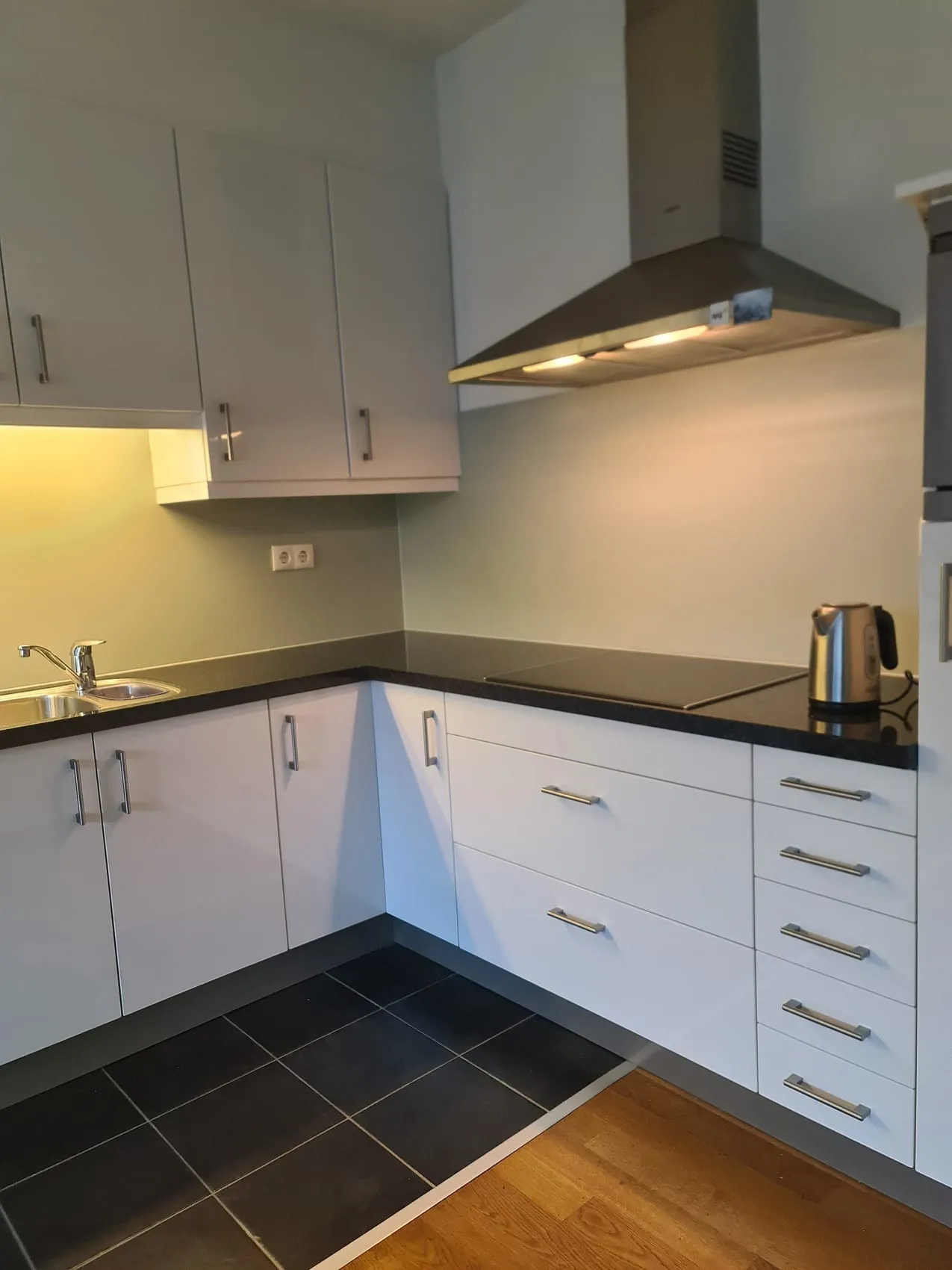 Frisse witte keuken met zwart werkblad en een naadloze licht groene rugwand