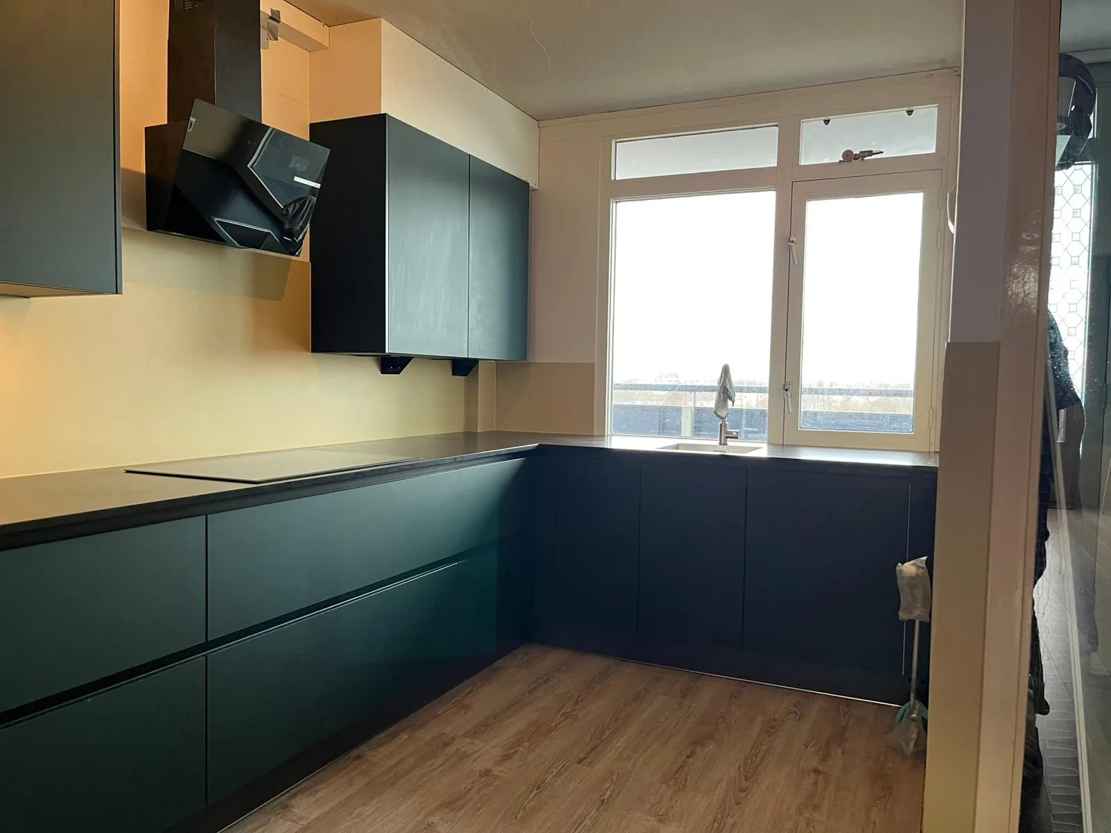 Een strakke crèmekleurige rugwand in een donkere keuken — na de plaatsing