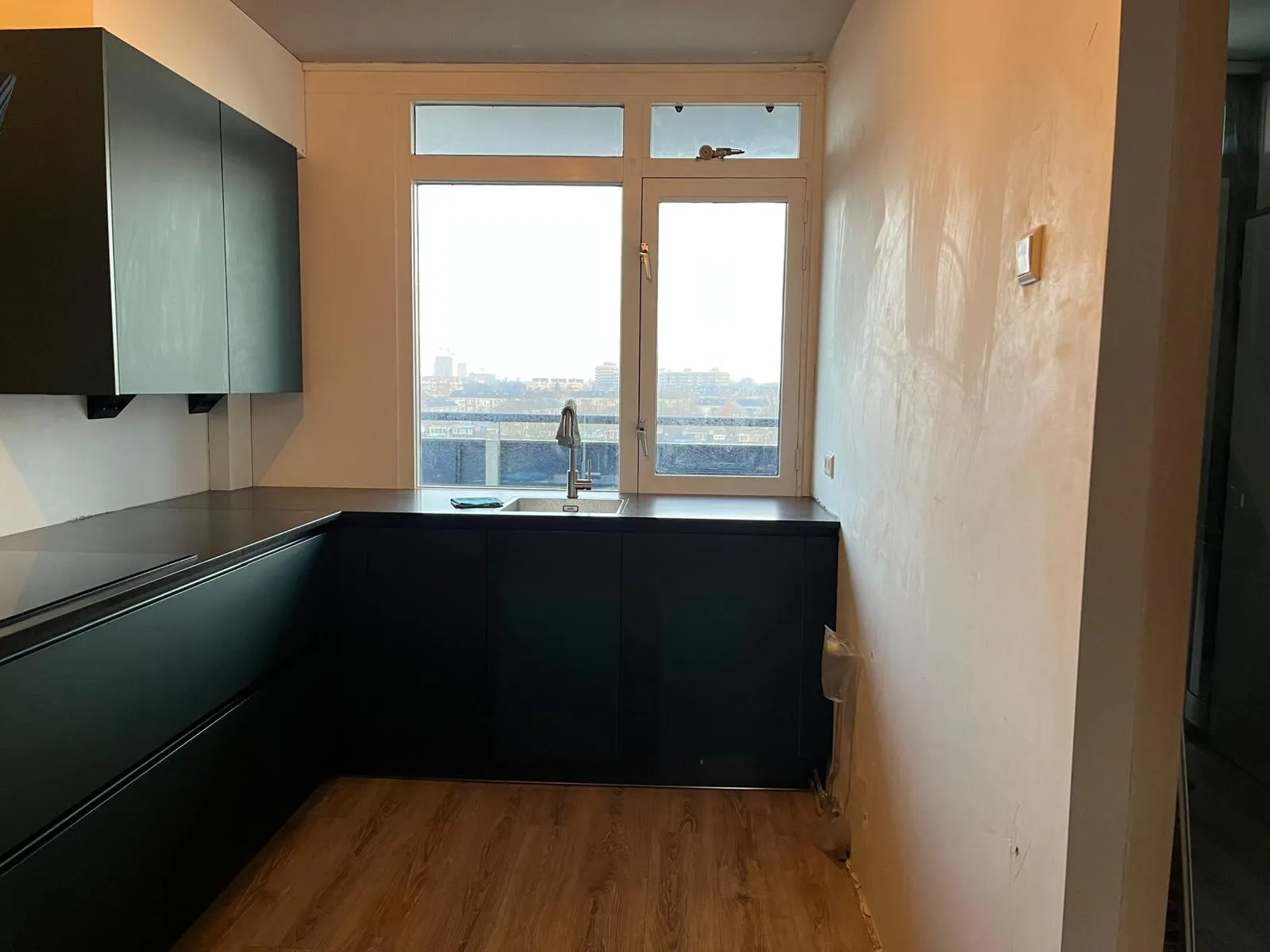 Een strakke crèmekleurige rugwand in een donkere keuken — voor de plaatsing