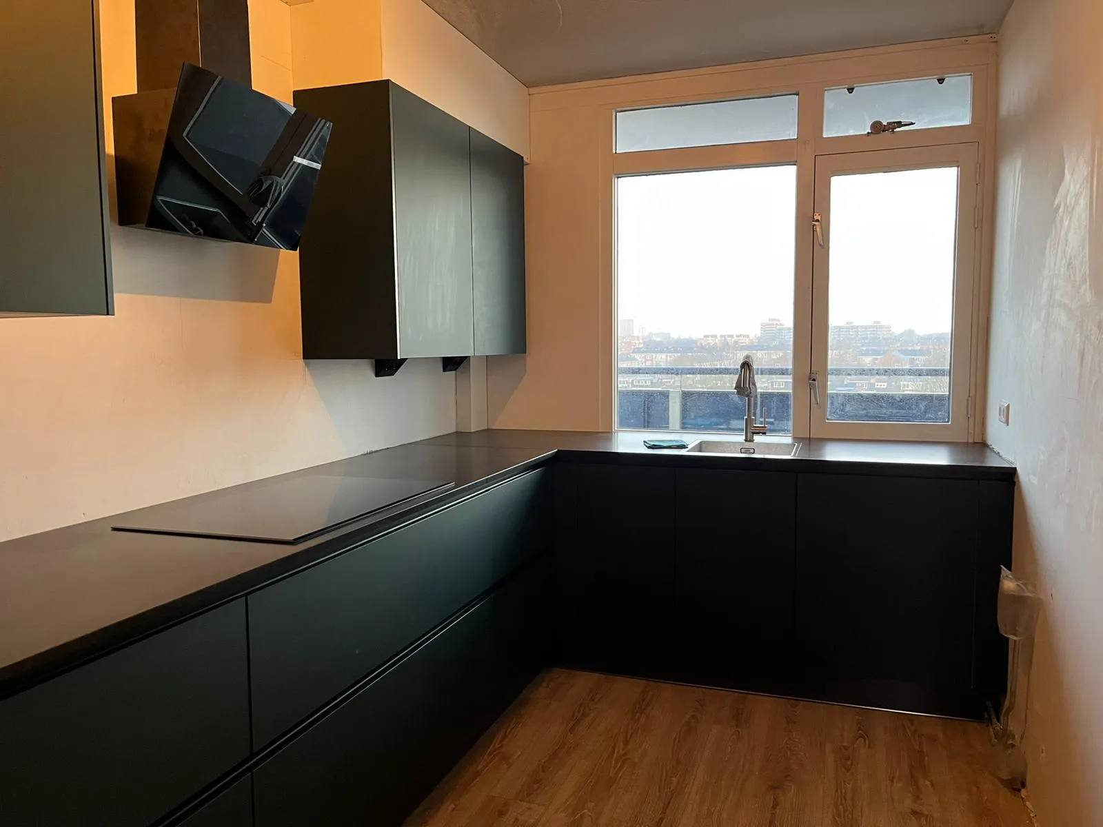 Een strakke crèmekleurige rugwand in een donkere keuken — voor de plaatsing